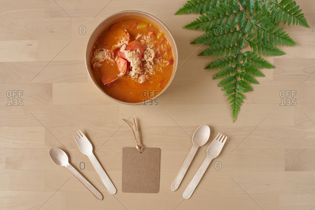 Top view of tasty rice and lobster with gravy served in cardboard bowl and placed on wooden table with disposable utensils