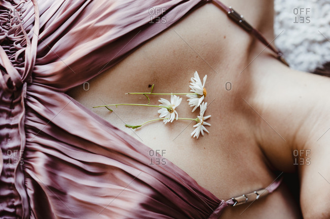 Crop unrecognizable female in stylish dress lying down demonstrating tender chamomile flowers attached with tape to chest