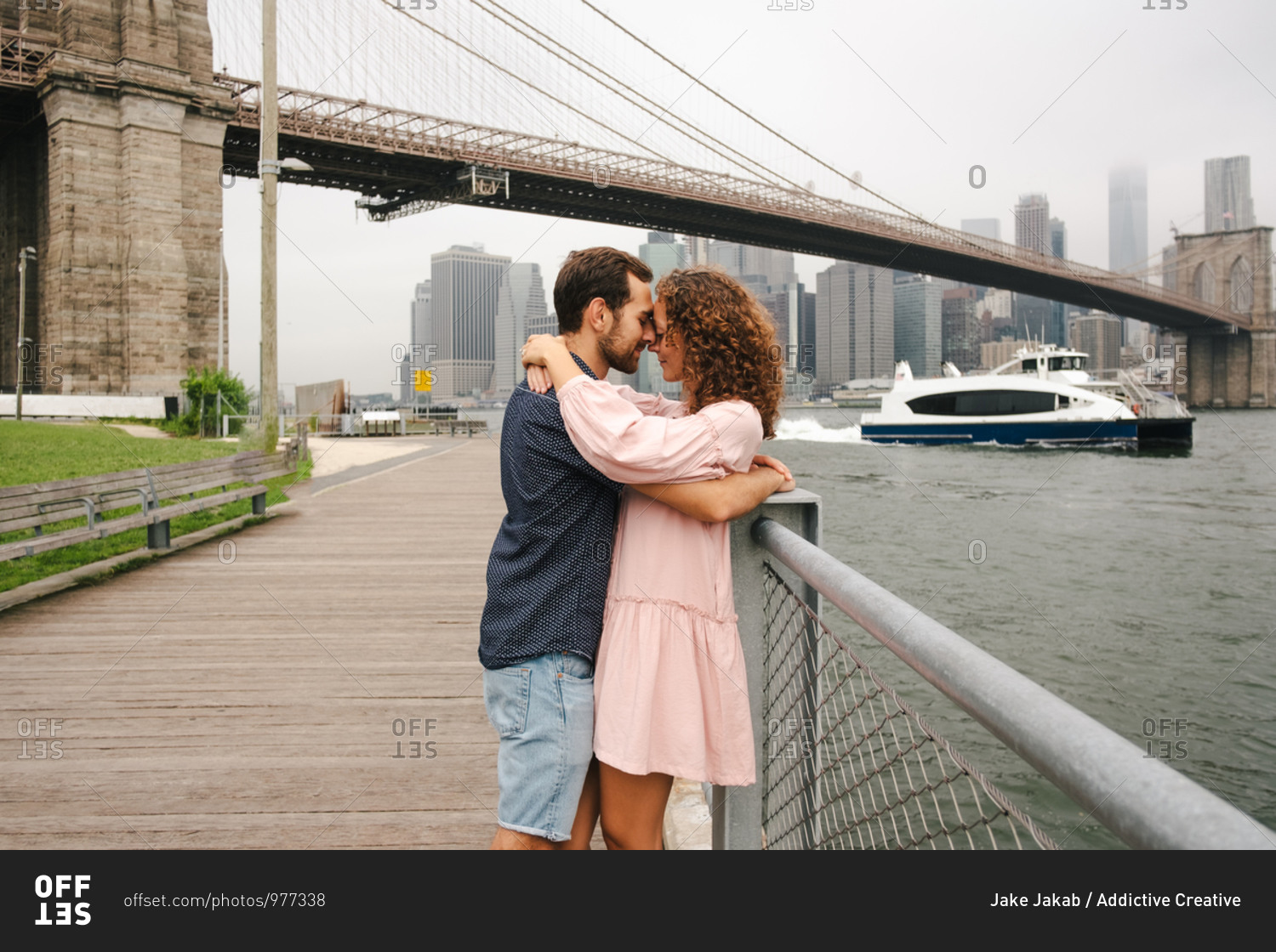 Side view of happy couple in casual wear standing with eyes closed on wooden promenade and hugging during city stroll near river while on vacations