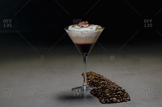 Roasted coffee beans and cocktail glass with yummy cappuccino with cream placed on concrete table