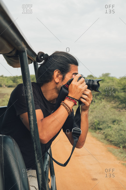 Happy traveling male with professional photo camera taking photos of wildlife during safari