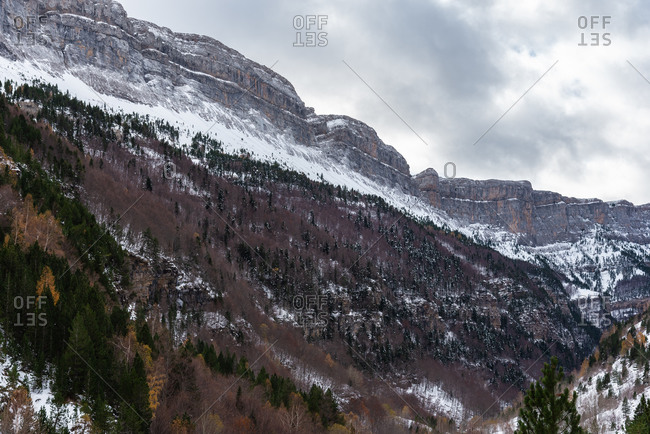 Forest and snowy mountain ridge against cloudy sky on stormy day in autumn countryside