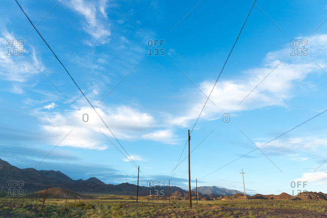 Low angle of electricity cables located in green field on background of magnificent sky