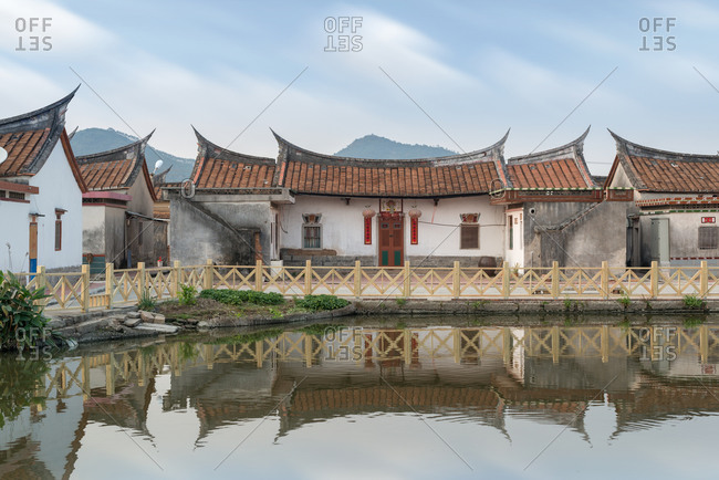 Small lake with wooden fences surrounded by traditional stone buildings with ornamental roofs in Daimei Village during sunrise