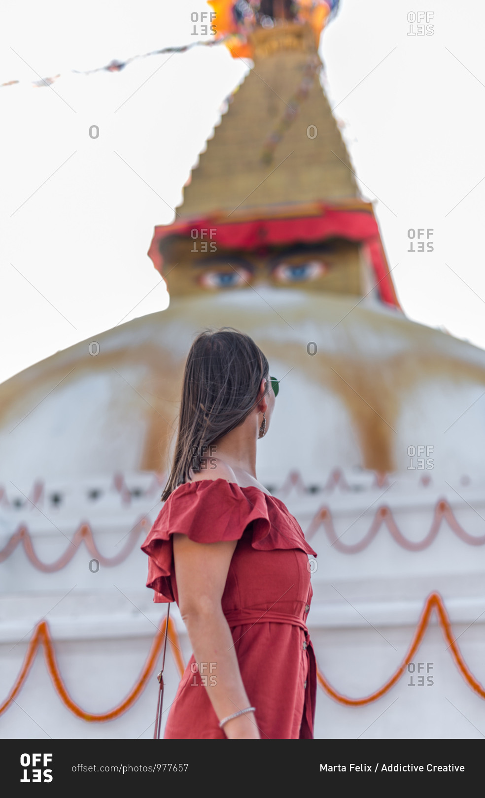 Side view of woman standing near Buddhist temple with decorative garlands and tower under cloudy sky in daylight