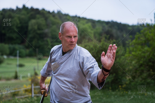 Determined middle aged male in kimono focusing and using sword while training alone in garden
