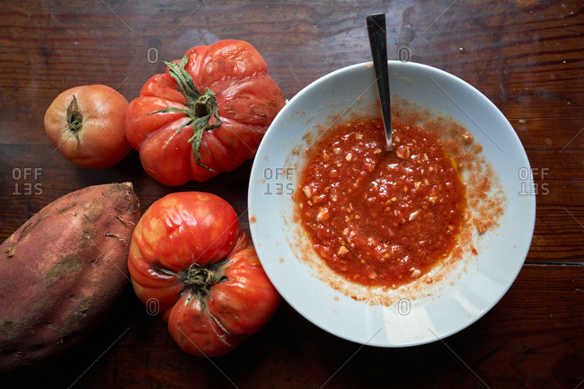 Stock photo of a dish with grated tomato and a teaspoon inside with two tomatoes on the side and a sweet potato