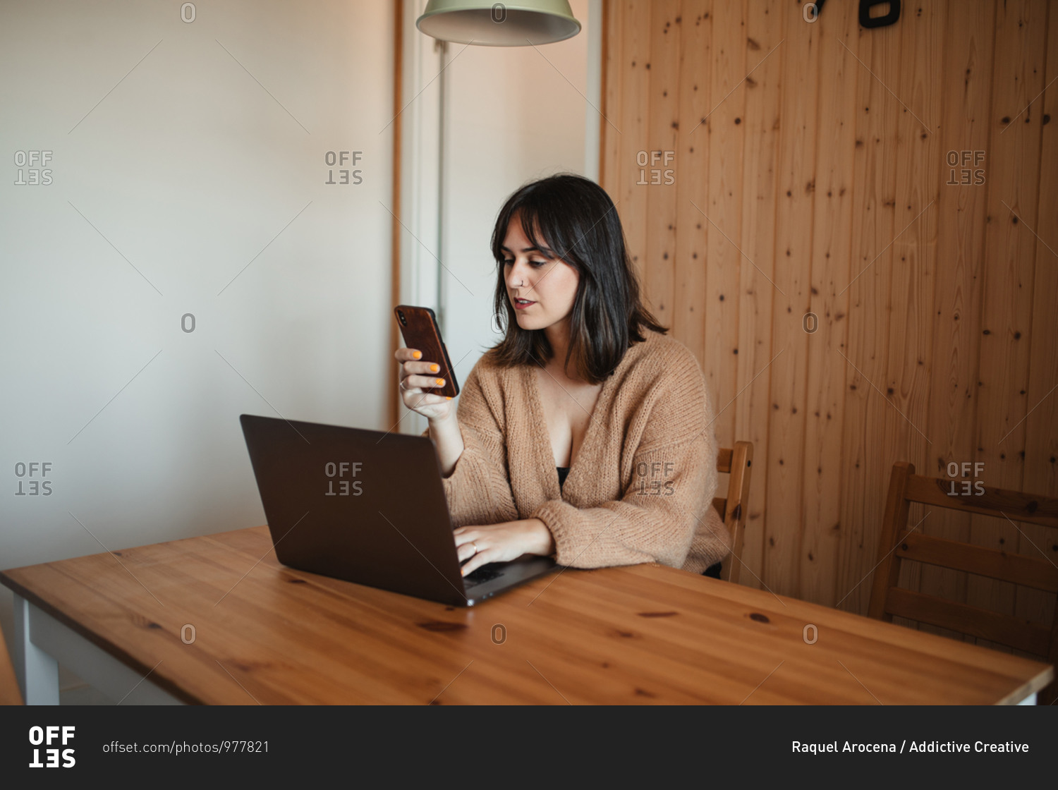 Side view of businesswoman sitting at table with laptop and messaging on smartphone during remote work