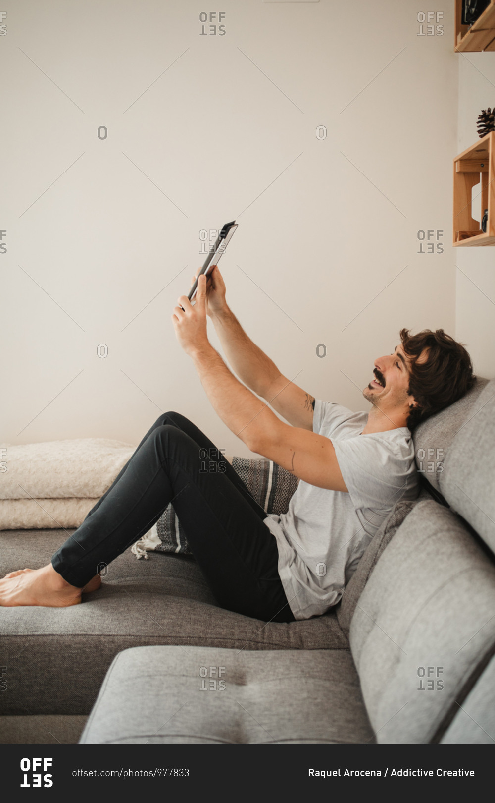 Relaxed male in casual wear sitting on couch and making video call on tablet while enjoying weekend at home