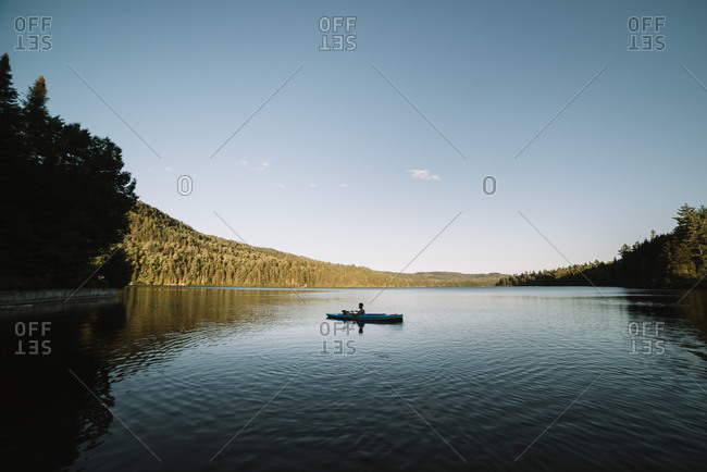 Silhouette of anonymous male traveler sitting on kayak and rowing during trip on calm river on cloudless day in La Mauricie National Park in Quebec, Canada