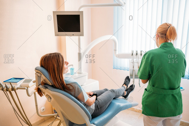 Focused middle aged professional doctor in green uniform examining oral cavity of woman in dentist chair