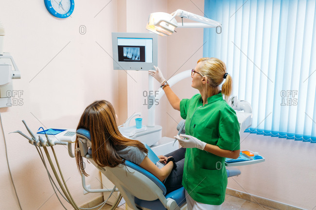 Adult woman in medical gloves and uniform explaining result of teeth X ray to female patient in office