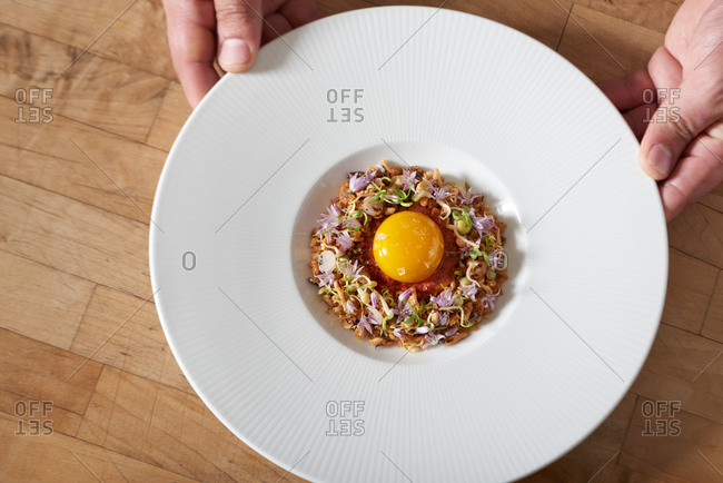 A dish of puffed rice with microgreens and edible flowers topped with an egg yolk and sea salt