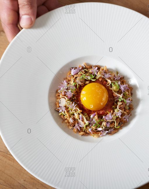 Puffed rice dish with microgreens and edible flowers topped with an egg yolk and sea salt