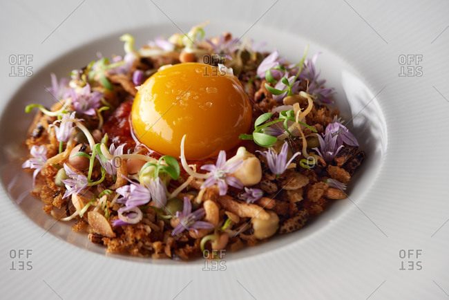 Close up of a puffed rice dish with microgreens and edible flowers topped with an egg yolk and sea salt