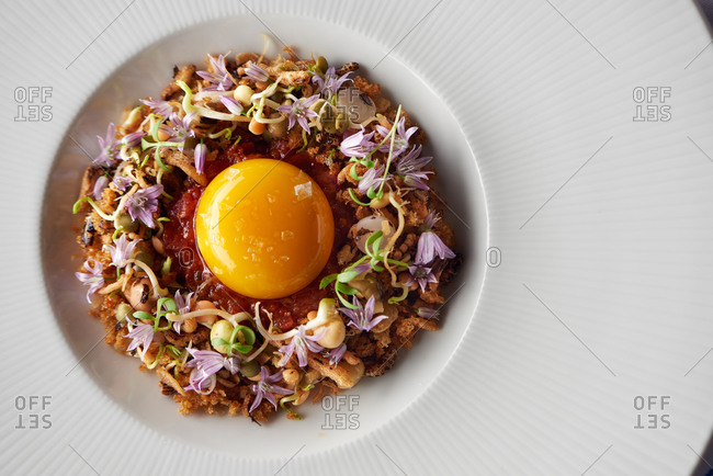 Overhead view of a puffed rice dish with microgreens and edible flowers topped with an egg yolk and sea salt