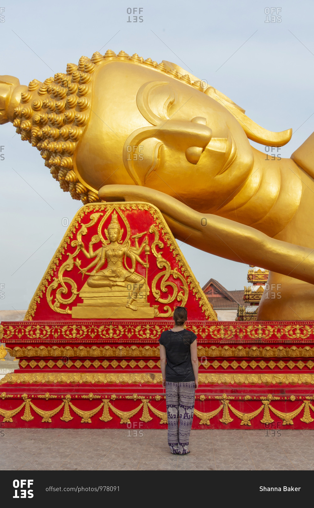 Woman looking at a giant, golden reclining Buddha statue in Vientiane, Laos