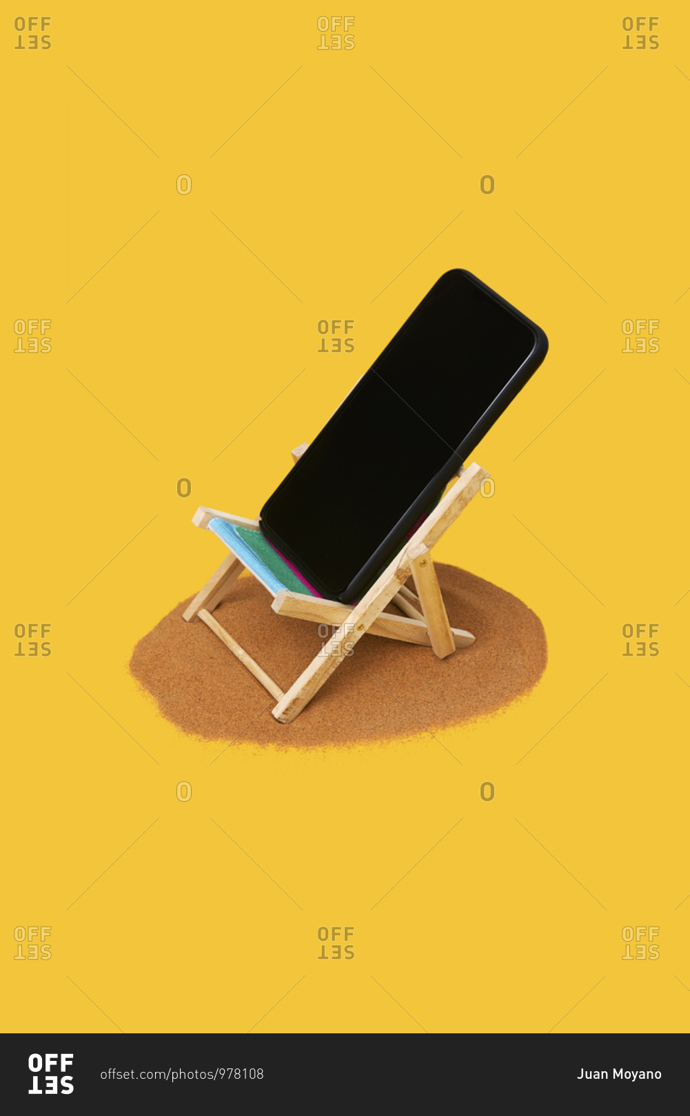 Smartphone in a small deck chair on a pile of sand on a bright yellow background