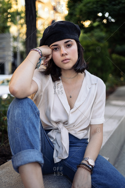 Young woman wearing a beret posing and looking at camera on a bench in the street