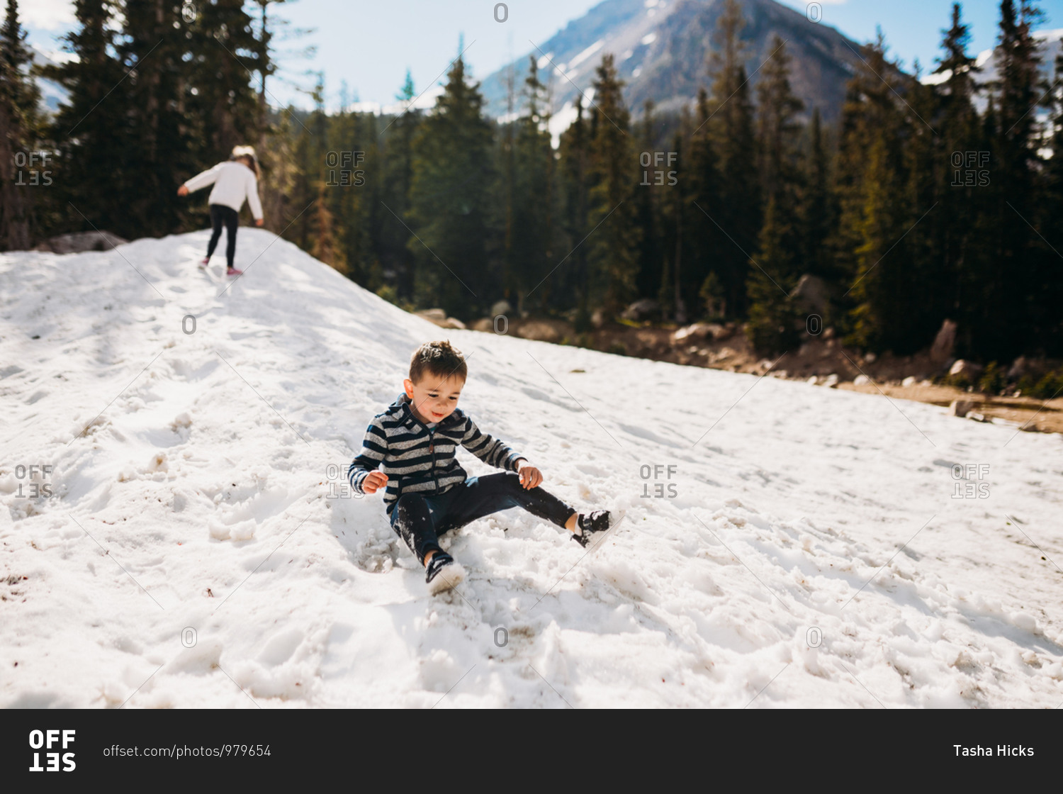 Happy toddler boy sliding down snow in the mountains stock photo - OFFSET