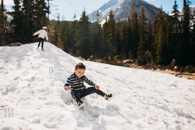 Happy toddler boy sliding down snow in the mountains stock photo
