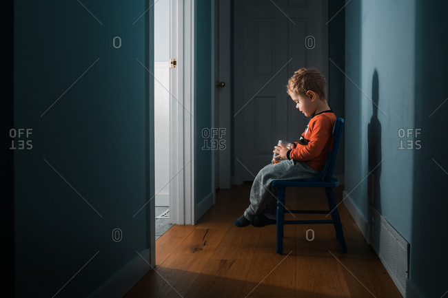 Young boy sitting on chair outside of bathroom door holding jar of treats