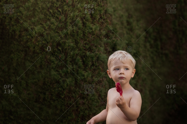 Toddler boy eating a popsicle in front of greenery