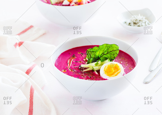 Two bowls of cold beetroot soup with boiled egg cucumber and green chip as a garnish