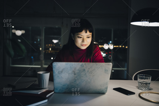 Confident young female professional using laptop while working late in creative workplace