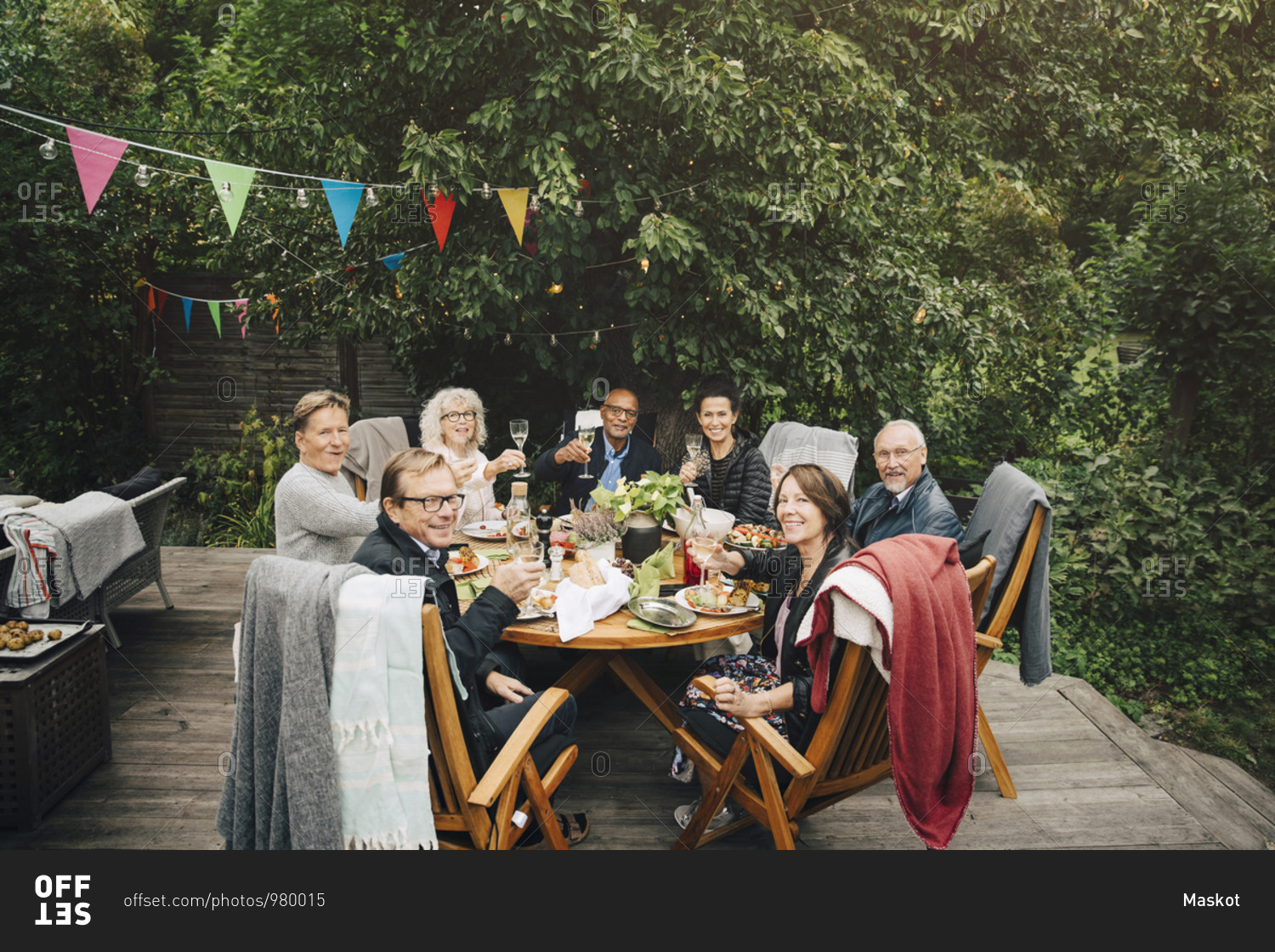 Portrait of smiling active senior men and women with celebratory toast sitting at dining table at back yard during party