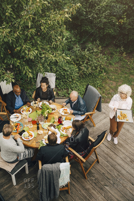 High angle view of woman serving meal to senior friends sitting at dining table during garden party at back yard