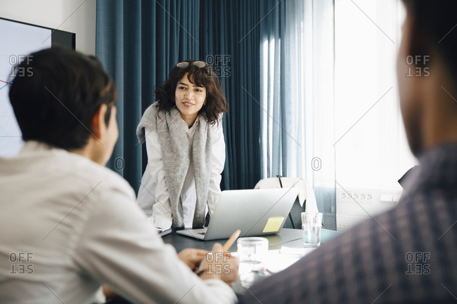Smiling businesswoman planning strategy with male colleagues in board room during meeting
