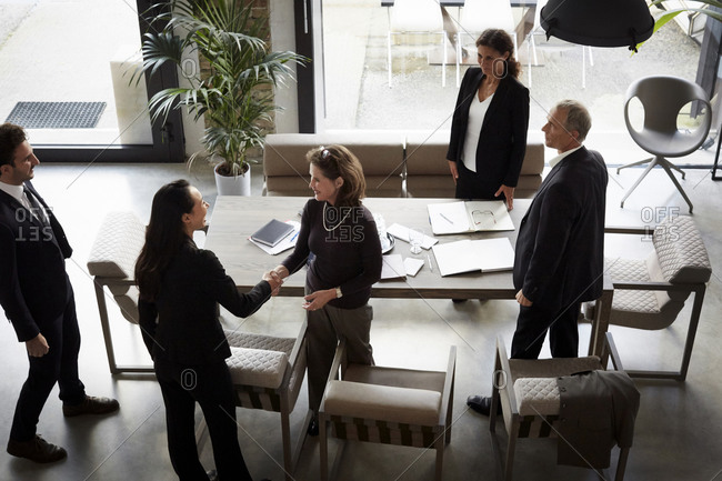 High angle view of female financial advisor greeting businesswoman while colleagues standing in office during meeting
