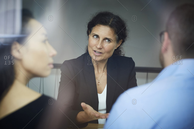 Confident mature female financial advisor discussing with businessman and businesswoman during meeting at office