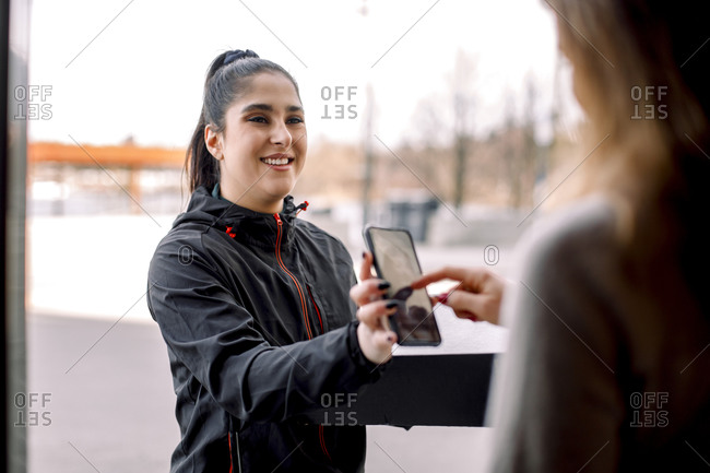 Woman signing on smart phone while receiving package from delivery woman