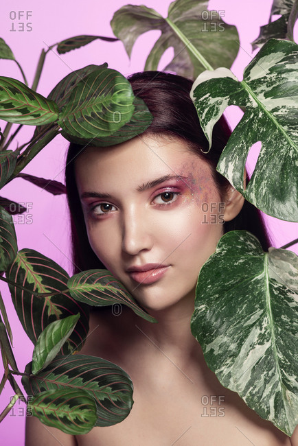 Portrait of a young woman with leafy plants in front of pink background
