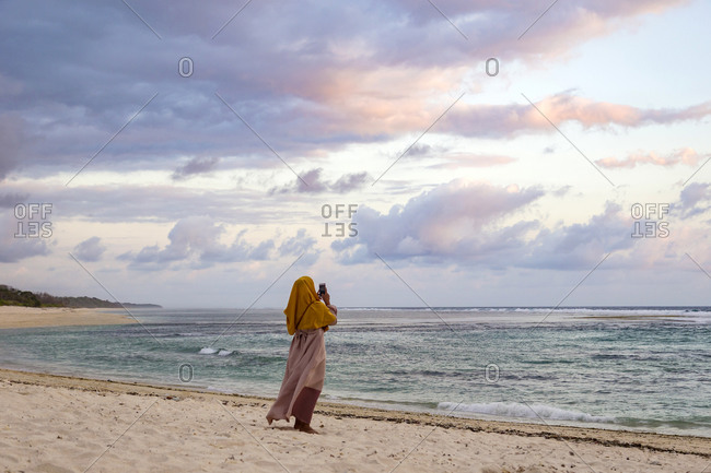 Woman photographing ocean coastline, Sumbawa, Indonesia