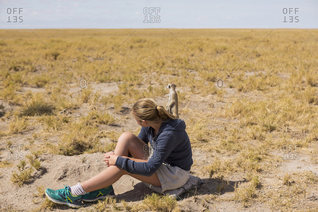 Twelve year old girl sitting watching meerkats emerge from their burrows, in the Kalahari desert.