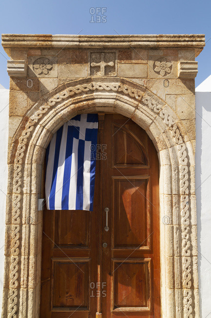 A Greek flag hangs under the stone archway in the doorway of one of the captain\'s houses of Lindos on Rhodes, Dodecanese, Greek Islands, Greece, Europe