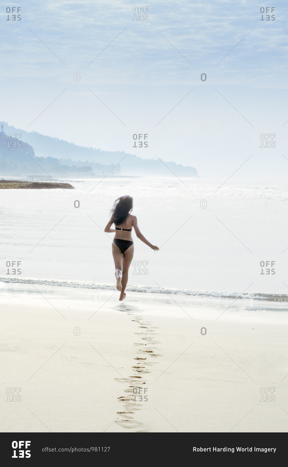 A woman solo traveller in a bikini running into the sea on a pristine tropical beach and leaving footprints, Indonesia, Southeast Asia, Asia