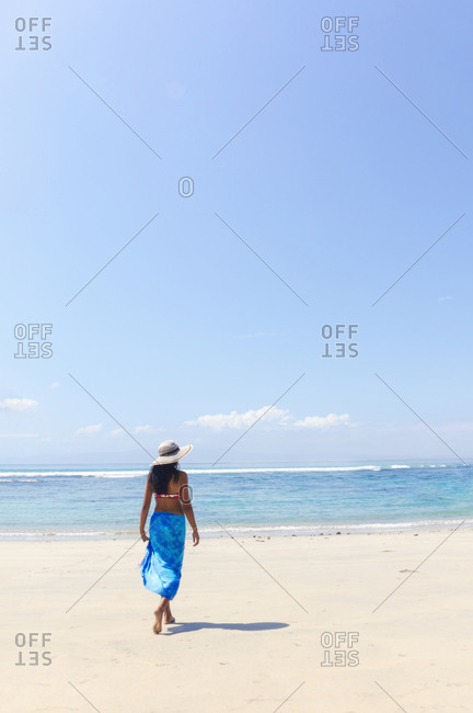 A young woman in a sunhat and shawl walking along a pristine tropical beach on Bali island, Indonesia, Southeast Asia, Asia