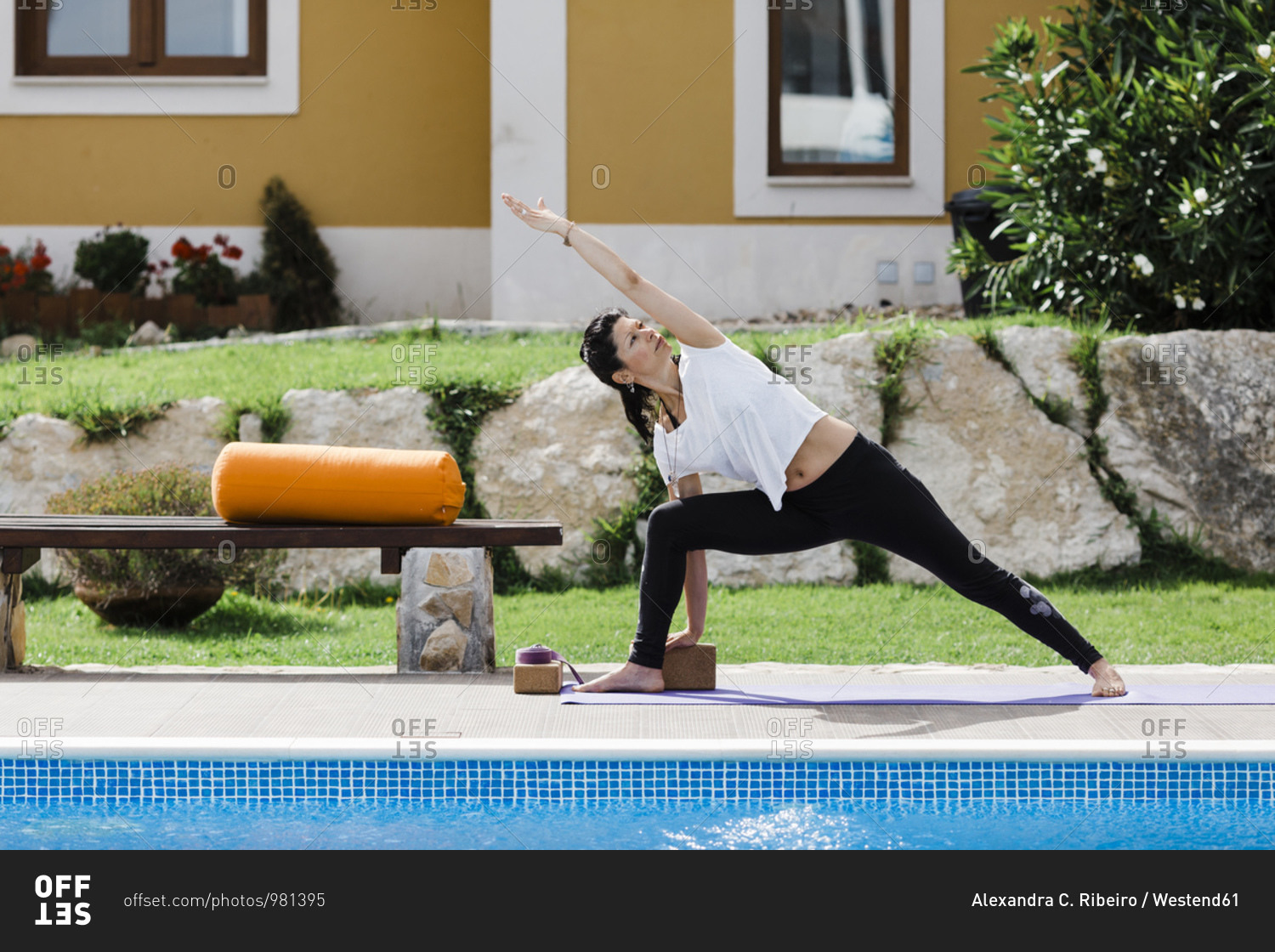 Mature woman practicing triangle position at poolside against house in yard