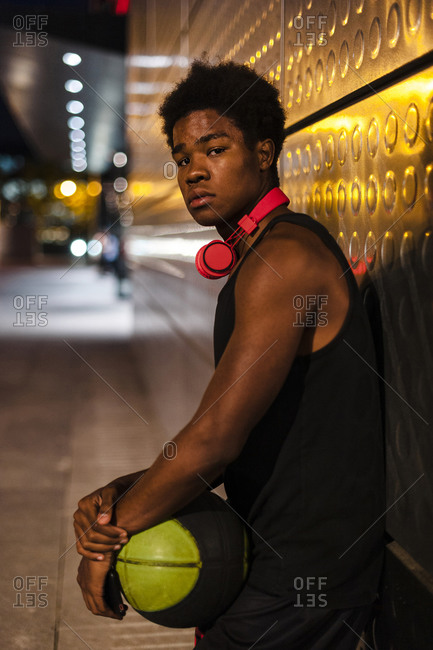 Portrait of a young man holding basketball at night in the city
