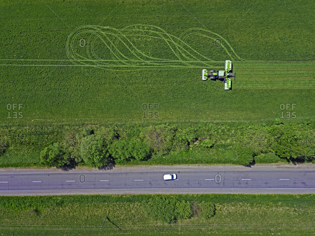Russia- Moscow Oblast- Aerial view of car driving along country road past tractor mowing green field