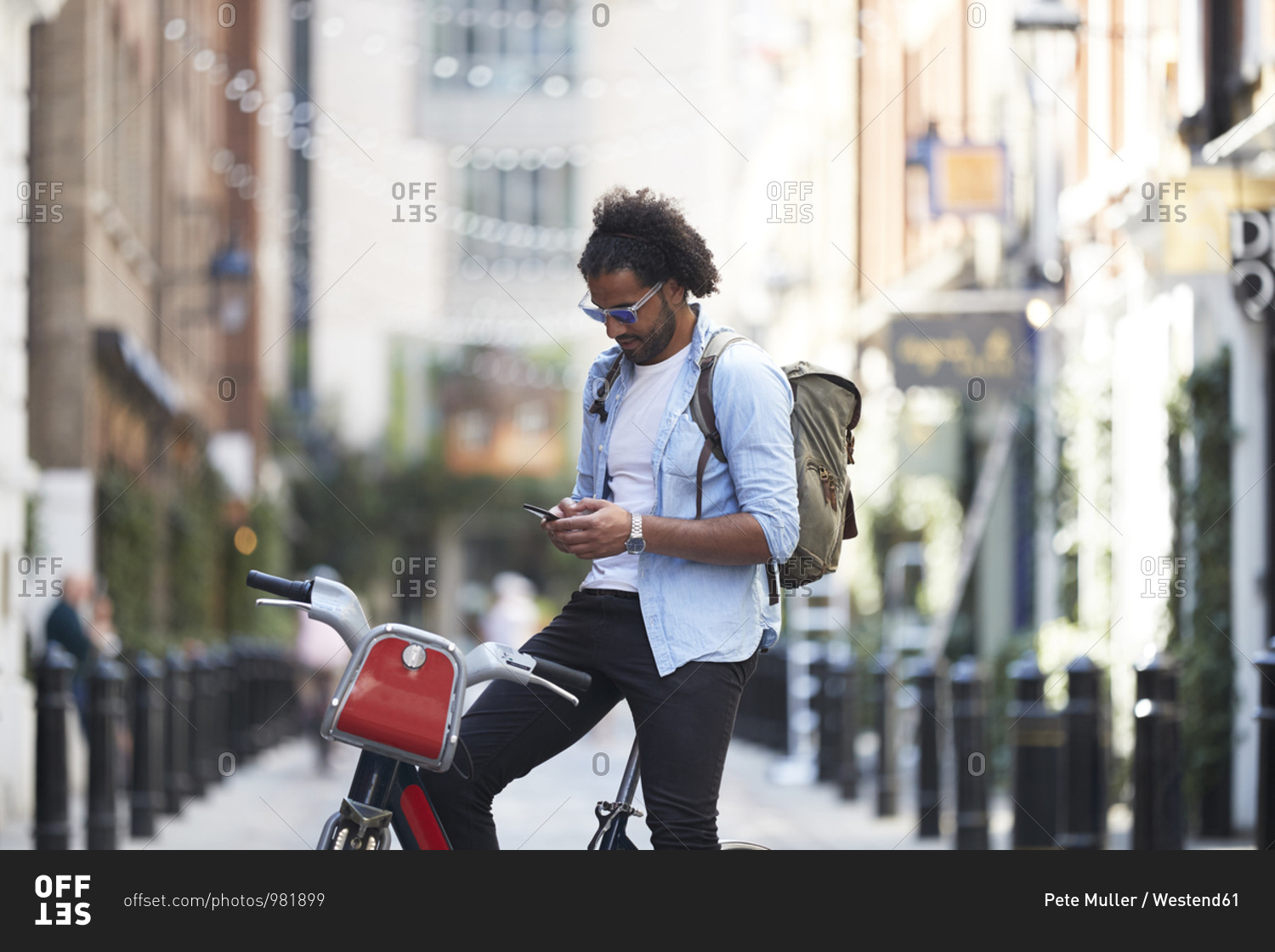 Young man with rental bike and backpack using cell phone in the city- London- UK