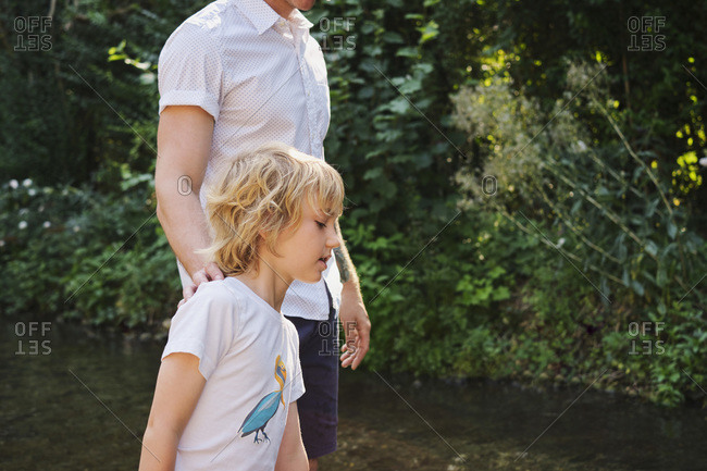 Father and son walking in stream during sunny day at forest