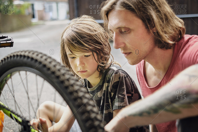 Father and son repairing bicycle at yard during sunny day