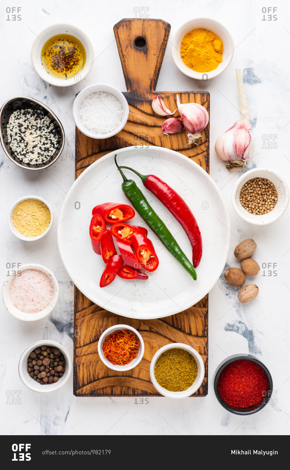 Red and green chili peppers on wooden cutting board with various spices over white background