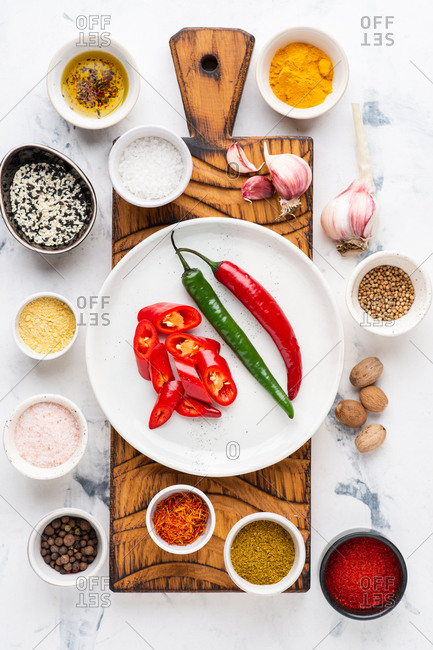 Red and green chili peppers on wooden cutting board with various spices over white background
