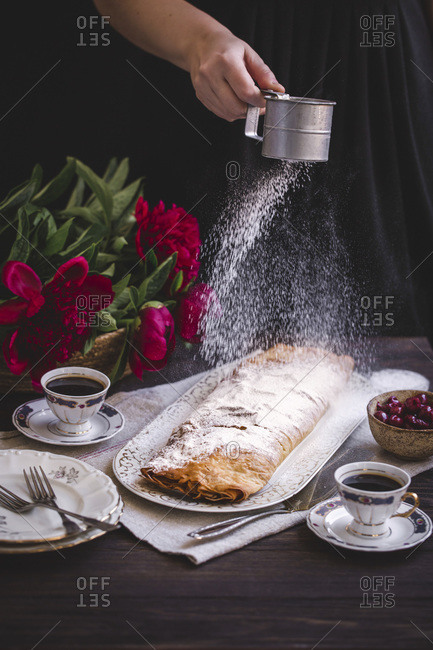 Woman dusting sour cherries strudel with powdered sugar